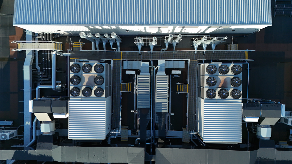 Rooftop HVAC installation with two large fan-cooled cooling units, extensive ductwork and metal walkways.