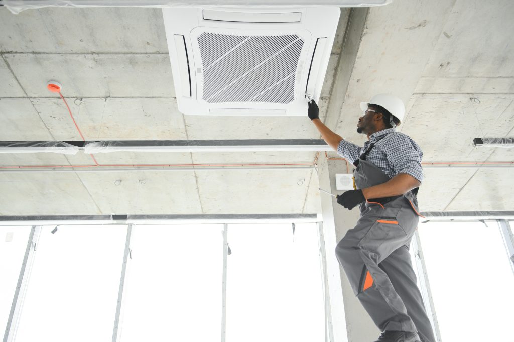 Construction worker in hard hat and gloves installs a ceiling HVAC unit in an industrial space